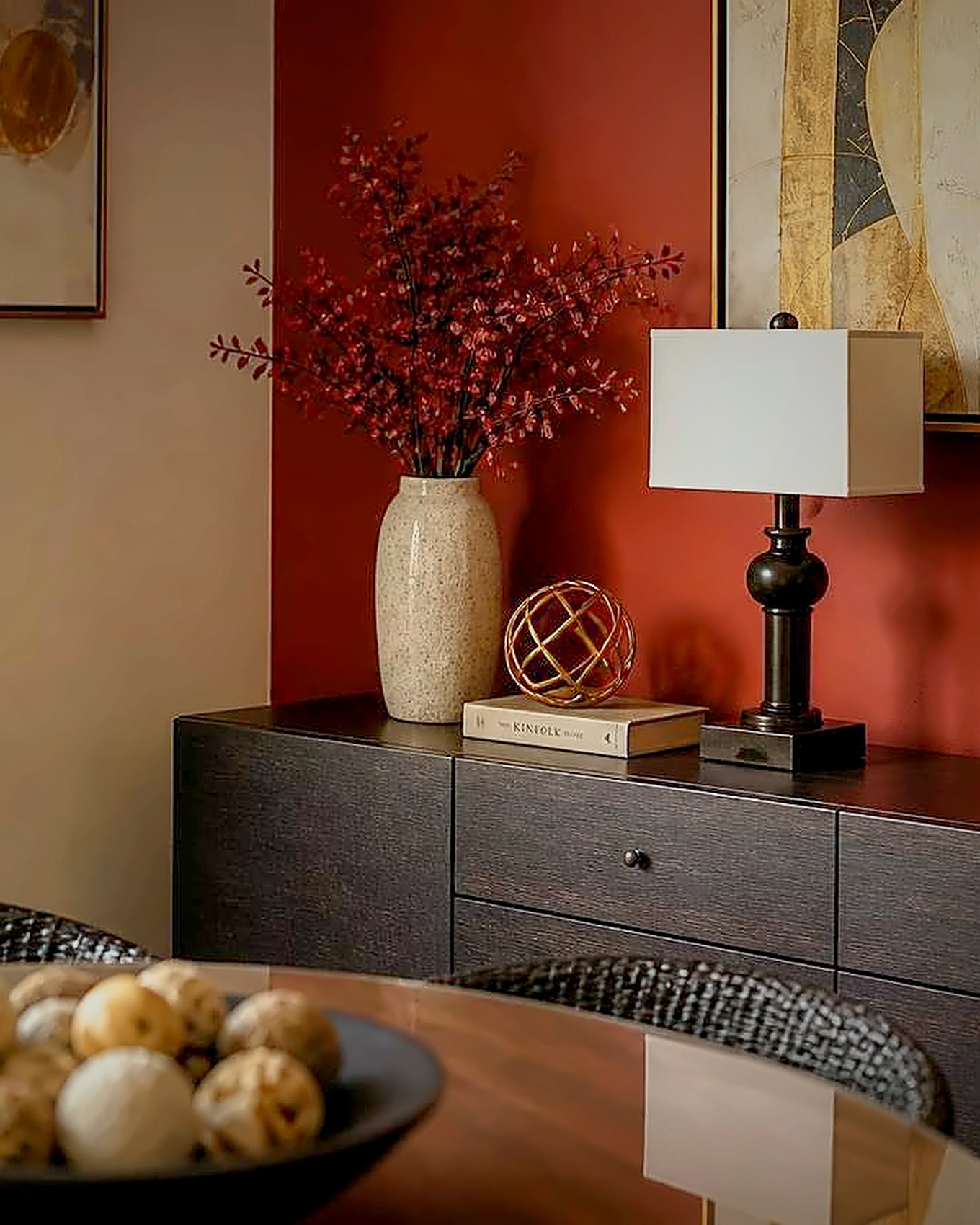 Hazmieh — red sideboard wall with a stone vase of red blossoms and a brass lamp in soft evening light