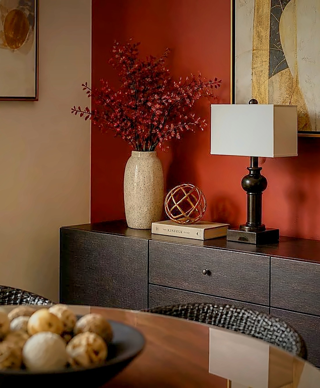 Hazmieh — red sideboard wall with a stone vase of red blossoms and a brass lamp in soft evening light