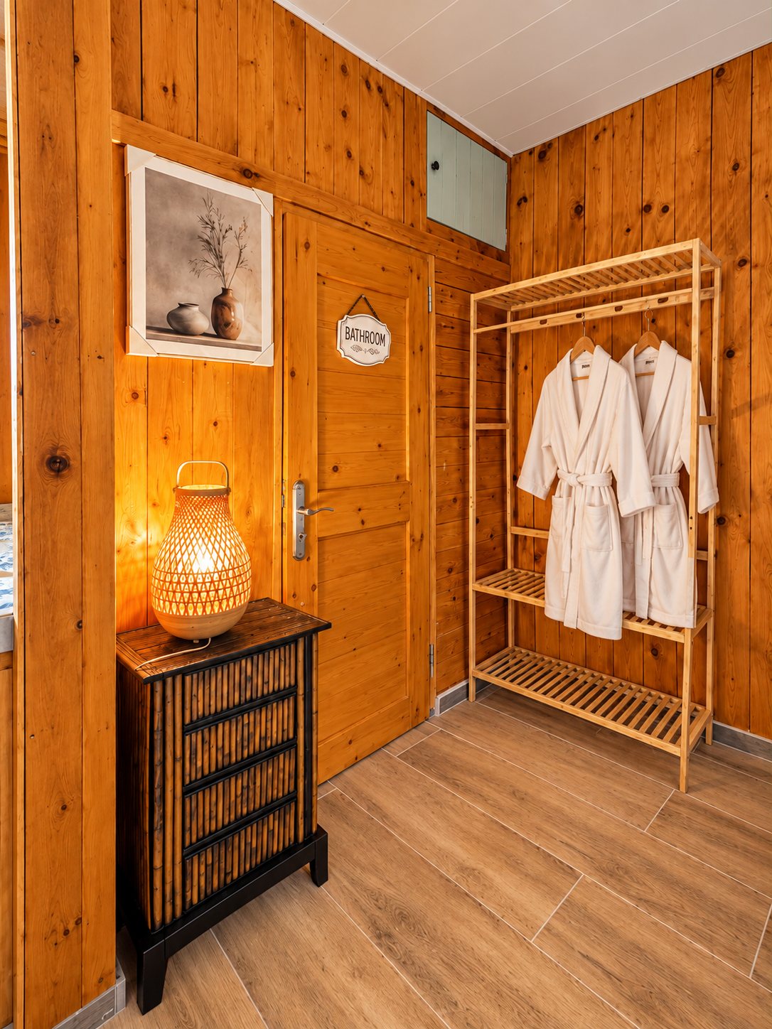 Bathroom entrance with bathroom door, bamboo lamp and bathrobes on the robe rack