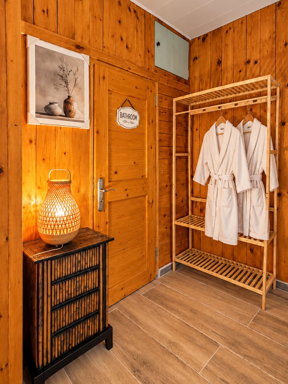 « Le Chalet » – Mountain Retreat: wood-panelled entry with a glowing bamboo lantern and two white bathrobes on a wooden rack beside the bathroom door